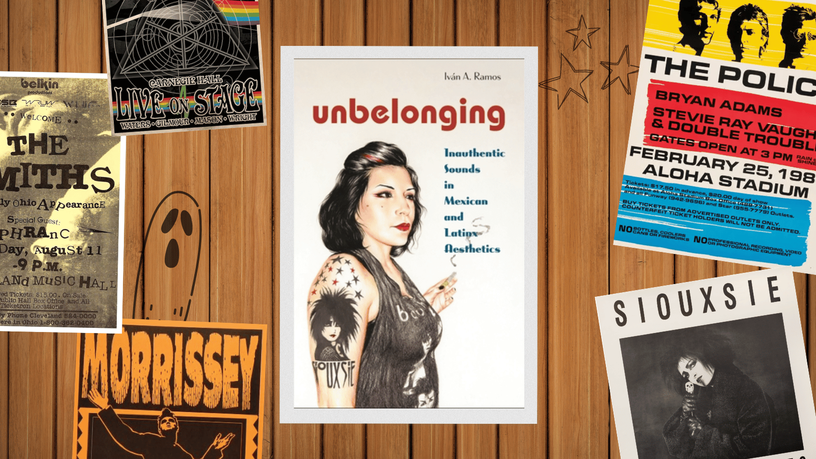 A framed image of the cover of Unbelonging on a wood panelled wall surrounded by sketches and images of posters from bands including Pink Floyd, The Smiths, The Police, Souxsie and the Banshees, and Morissey
