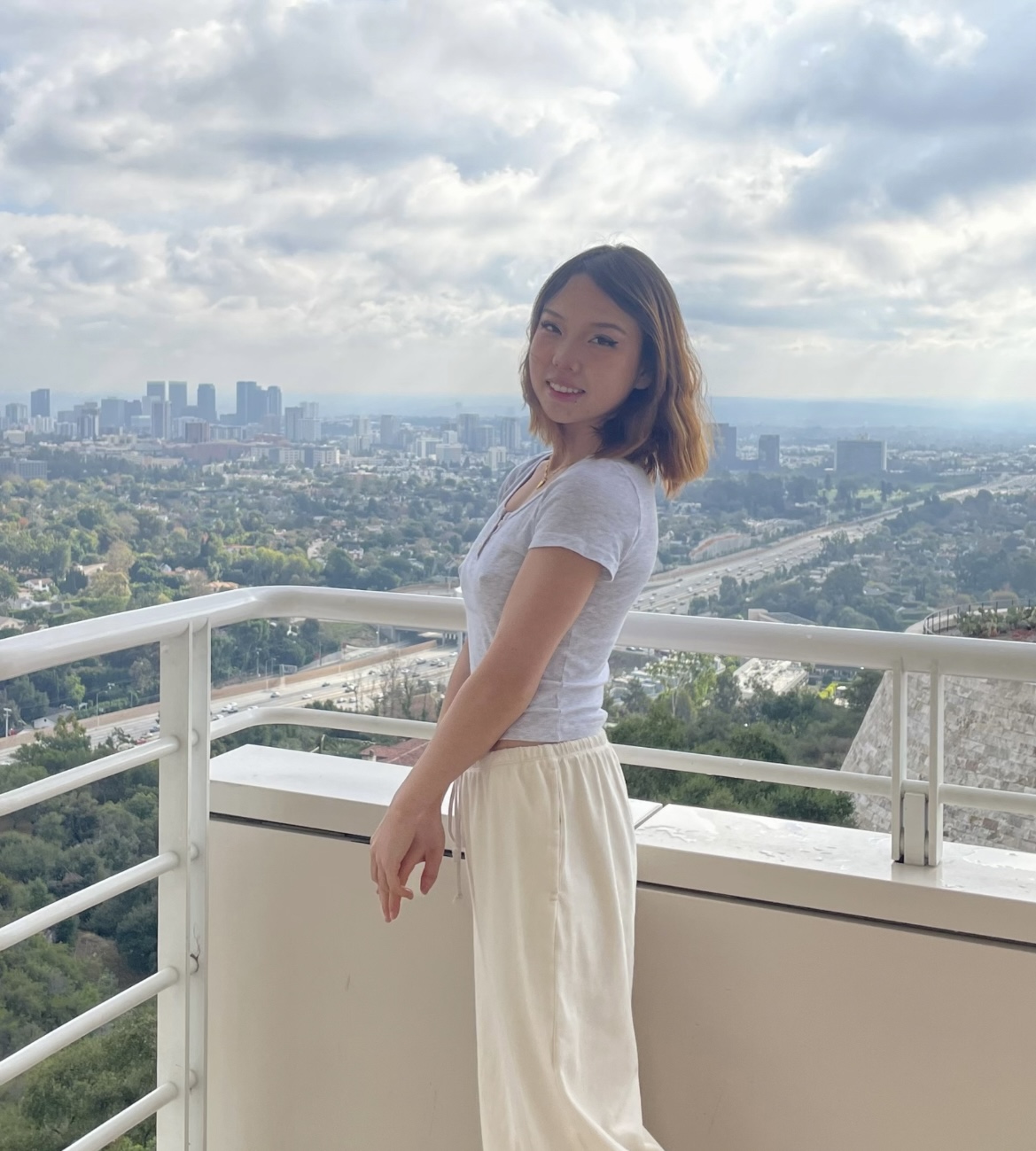 A woman poses on a balcony overlooking a cityscape