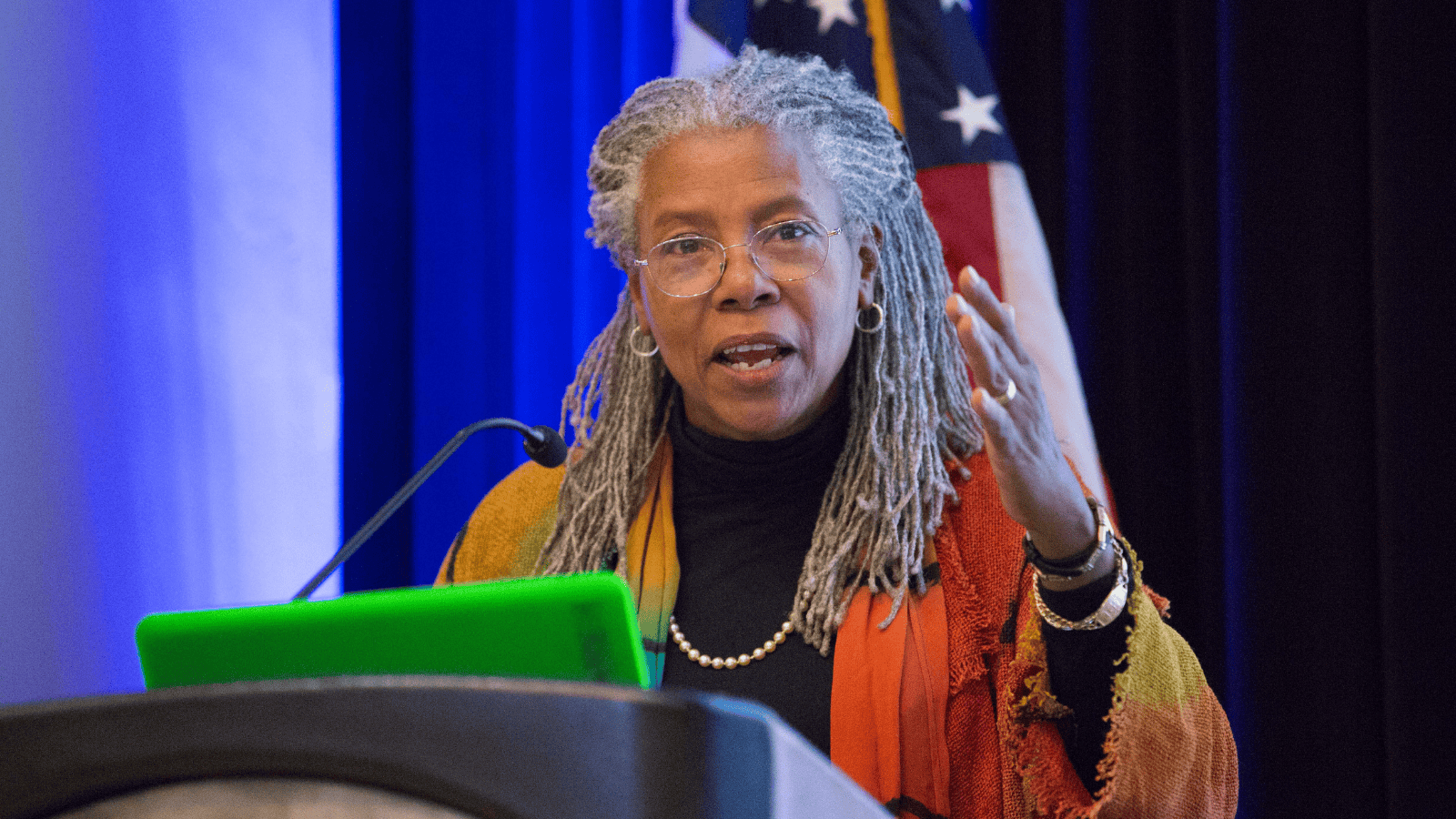 Image of Augusta Lynn Bolles, a black woman with gray dreadlock, giving a speech at a podium
